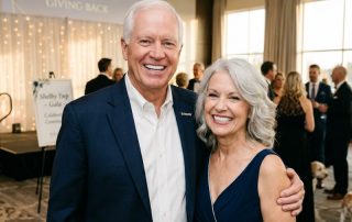 A candid photograph of a happy senior couple with bright, natural-looking smiles, showcasing beautiful partial dentures, at a social gathering.